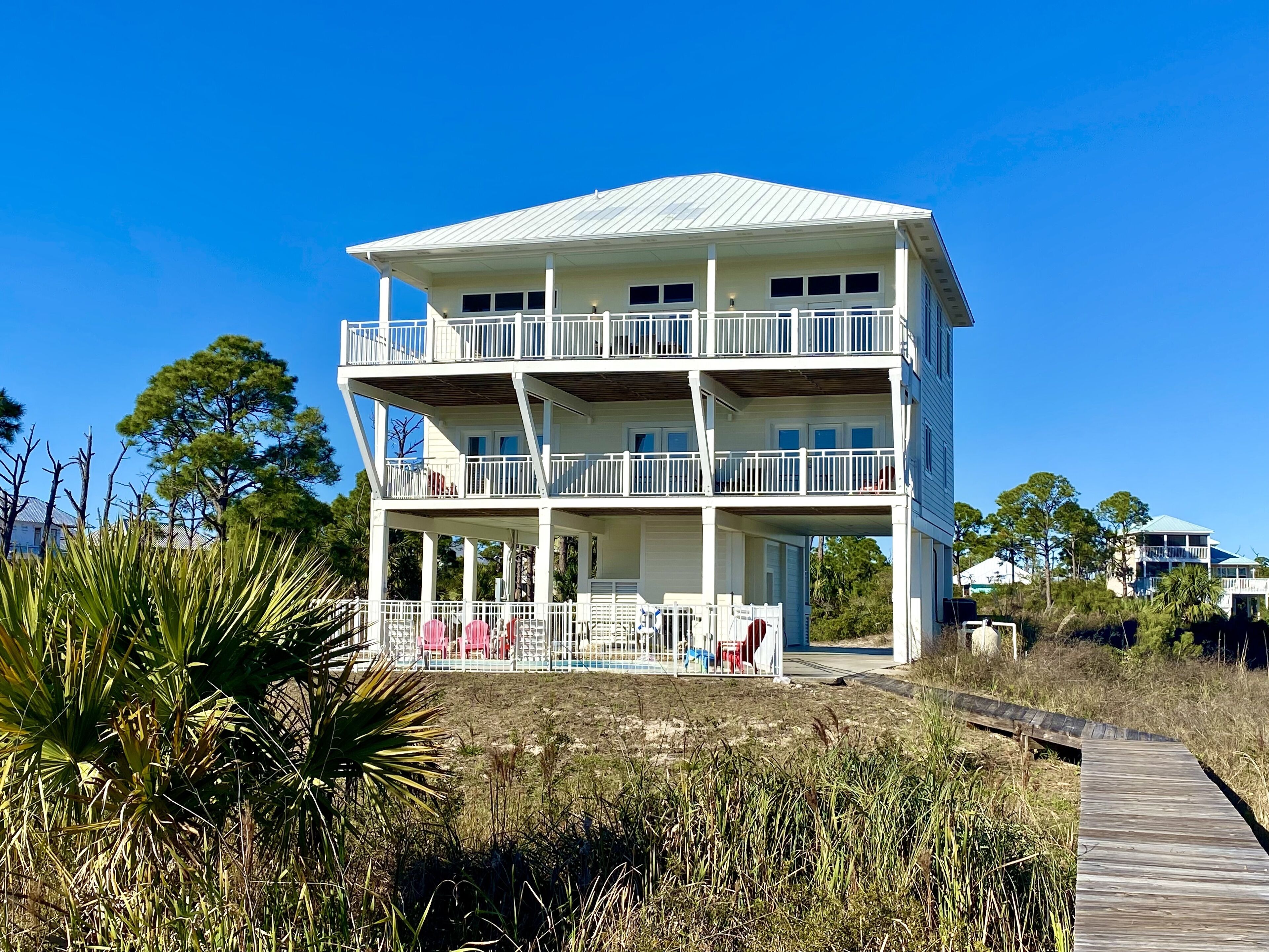 Un bâtiment à deux étages situé en bord de mer, doté de balcons, d’une véranda et d’une passerelle en bois menant à l’entrée.