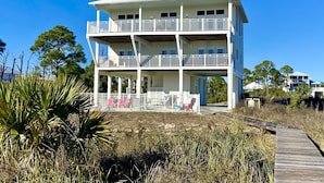 Un edificio frente a la playa de dos pisos con balcones, un porche cubierto y un paseo marítimo de madera que lleva a la entrada.