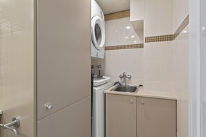 Ein kleines Badezimmer mit Waschmaschine, Waschbecken und Dusche.