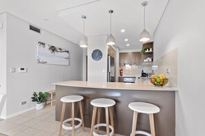 A modern kitchen with a central island, bar stools, pendant lighting, and a clock on the wall.