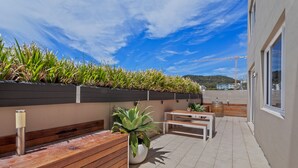 A rooftop terrace with a wooden bench, a table, and potted plants. - Carrington Nelson Bay (Nelson Bay)