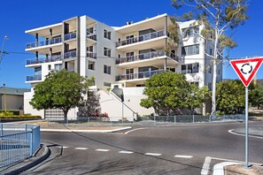 Un immeuble résidentiel à plusieurs étages, doté de balcons, situé près d’un rond-point et d’un panneau de signalisation.