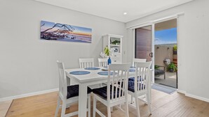 A dining area with a white table and chairs, a painting on the wall, and a view through an open door. - Carrington Nelson Bay (Nelson Bay)