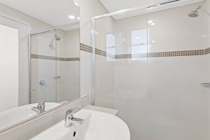 A modern bathroom with a glass-enclosed shower, a white sink, and a mirror.
