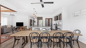 A modern kitchen with a central island, a dining area with a wooden table and chairs, and a living room with a sofa and TV.
