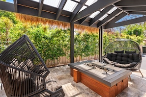 A covered outdoor seating area with a table and two chairs, surrounded by lush greenery.