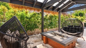 An outdoor patio with a wooden table, two black wicker chairs, and a hanging chair.