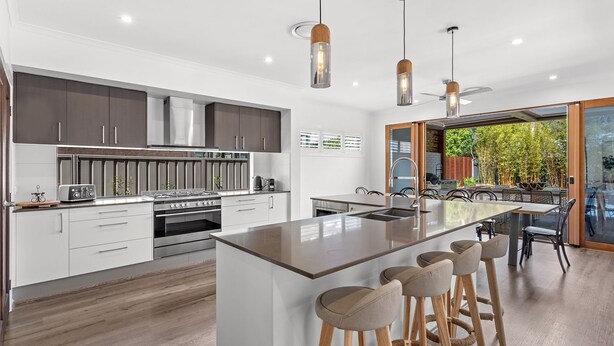 A modern kitchen with a central island, stainless steel appliances, and a dining area with outdoor seating.