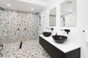 A modern bathroom with a terrazzo shower wall, two black vessel sinks, and a large mirror above the vanity.