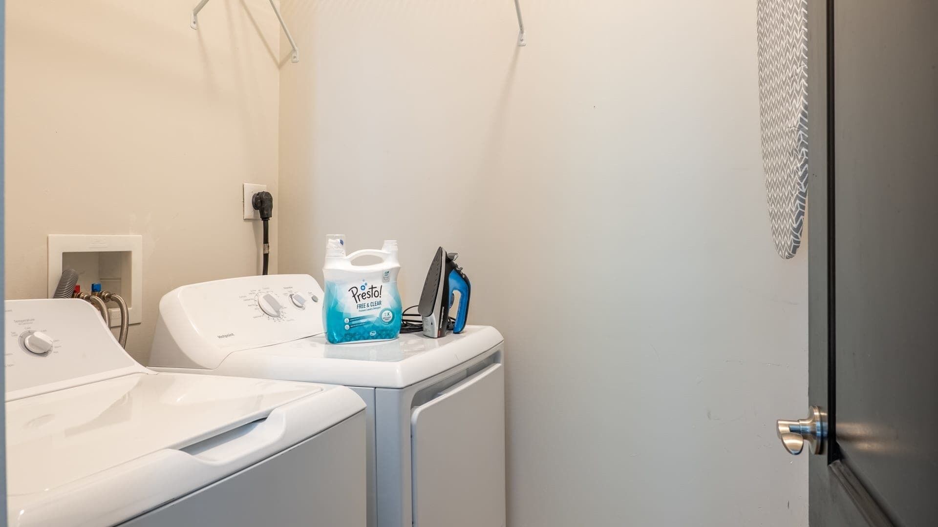 Ein Waschbereich mit Waschmaschine, Bügeleisen und einer Flasche Prestar Waschmittel.