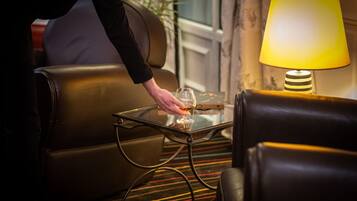 Eine Person stellt ein Glas auf einen Glastisch neben eine Couch in einem Zimmer mit einer Lampe.