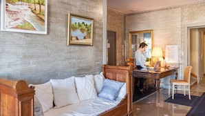 Ein Hotelzimmer mit einer Holzsofa, einem Schreibtisch mit einem Laptop, einem Sessel und zwei gerahmten Bildern an der Wand.