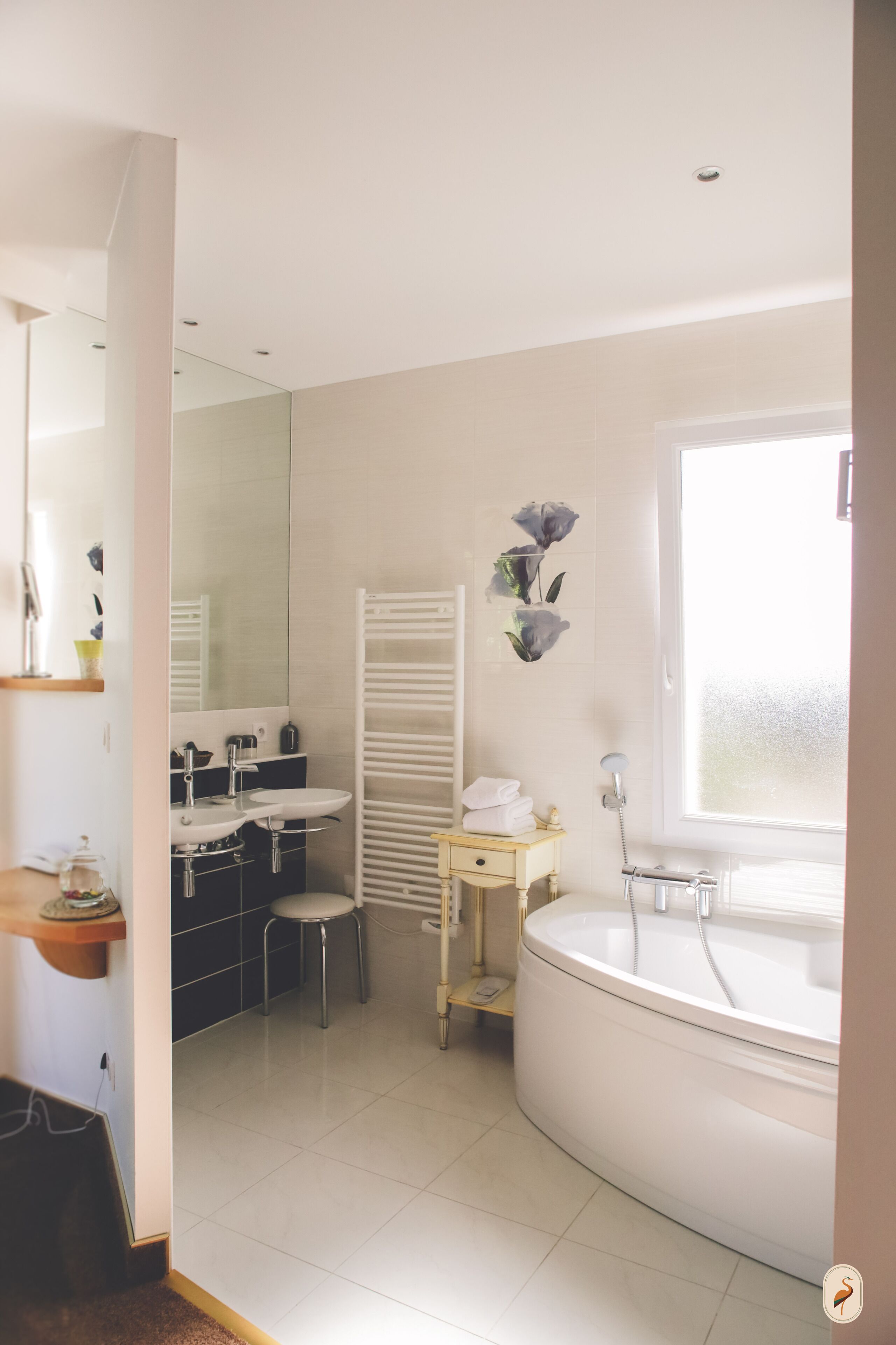Ein modernes Badezimmer mit einer großzügigen Badewanne, einem Waschbecken und einem Spiegel. Handtuchhalter und ein kleiner Hocker sind ebenfalls vorhanden.