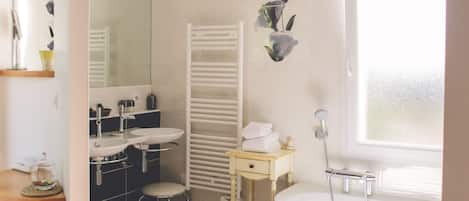 Un baño moderno con una bañera grande, un lavabo y un espejo. Hay un perchero y un taburete pequeño.
