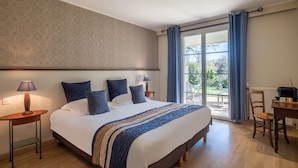 Ein Schlafzimmer mit einem großen Bett, einem Nachttisch mit Lampe, einem Holzstuhl und Blick ins Freie durch eine Glastür.