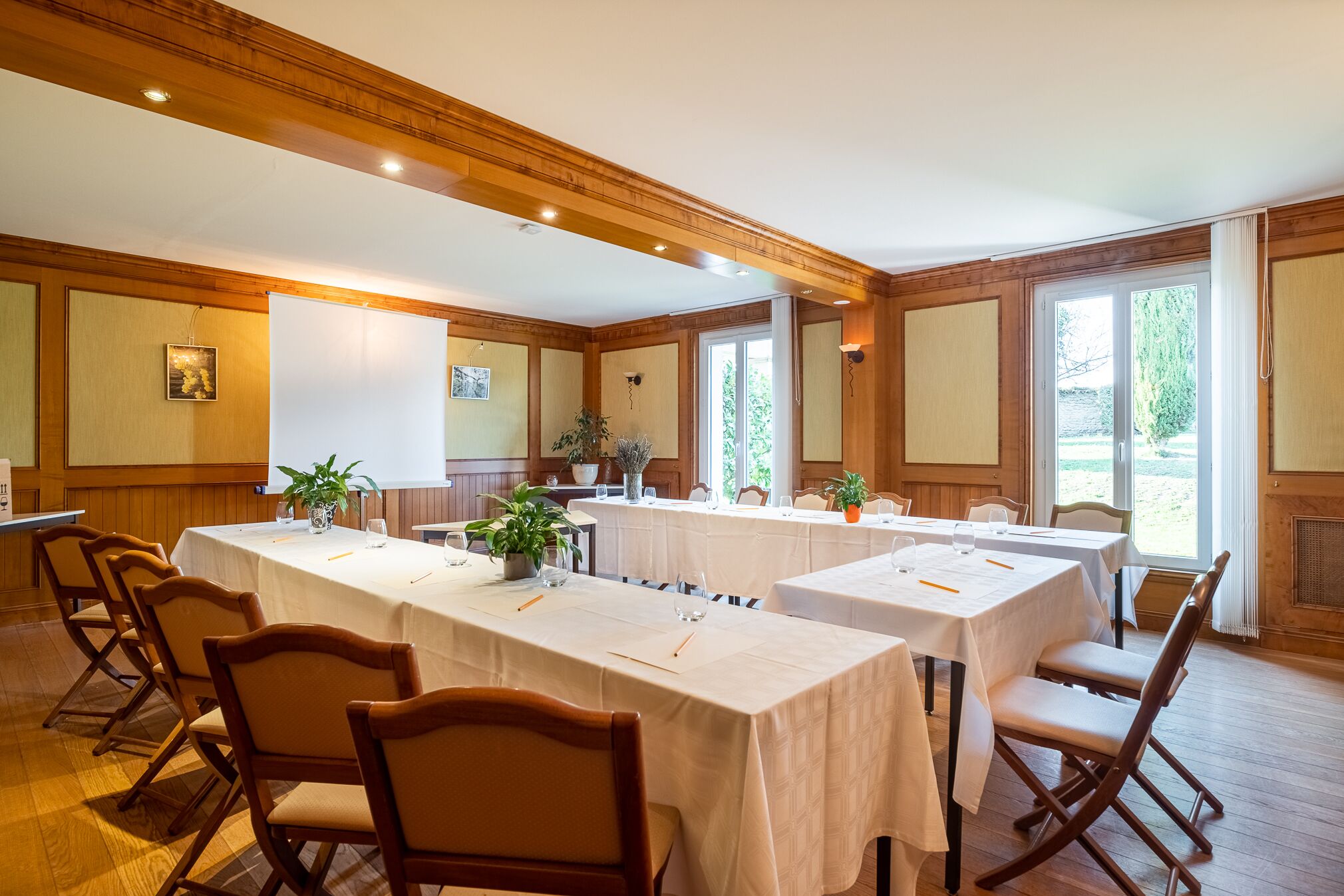 Une salle de conférence avec des panneaux de bois, des tables blanches et des chaises.