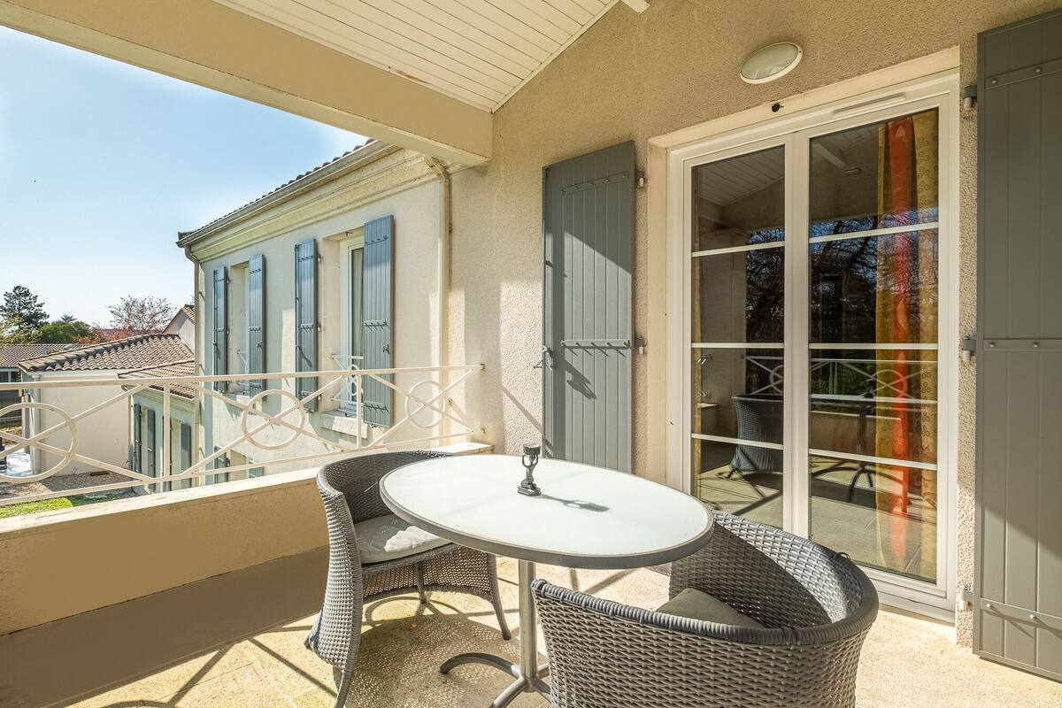 Un balcón con mobiliario de mimbre, una mesa de vidrio y vistas a edificios cercanos.