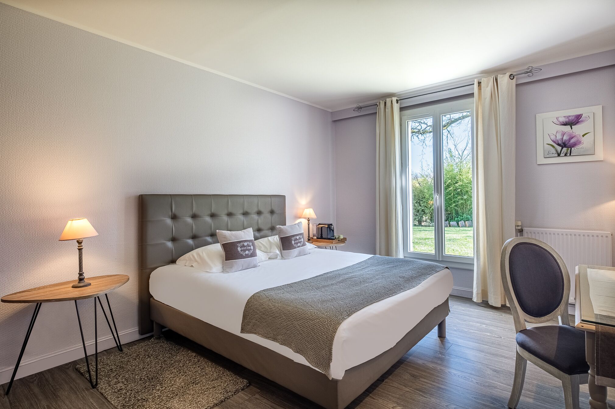 Un dormitorio con una cama grande, una mesita de noche con lámpara, una silla y vistas al exterior a través de una ventana.