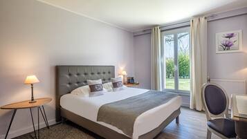 Un dormitorio con una cama grande, una mesita de noche con lámpara, una silla y vistas al exterior a través de una ventana.
