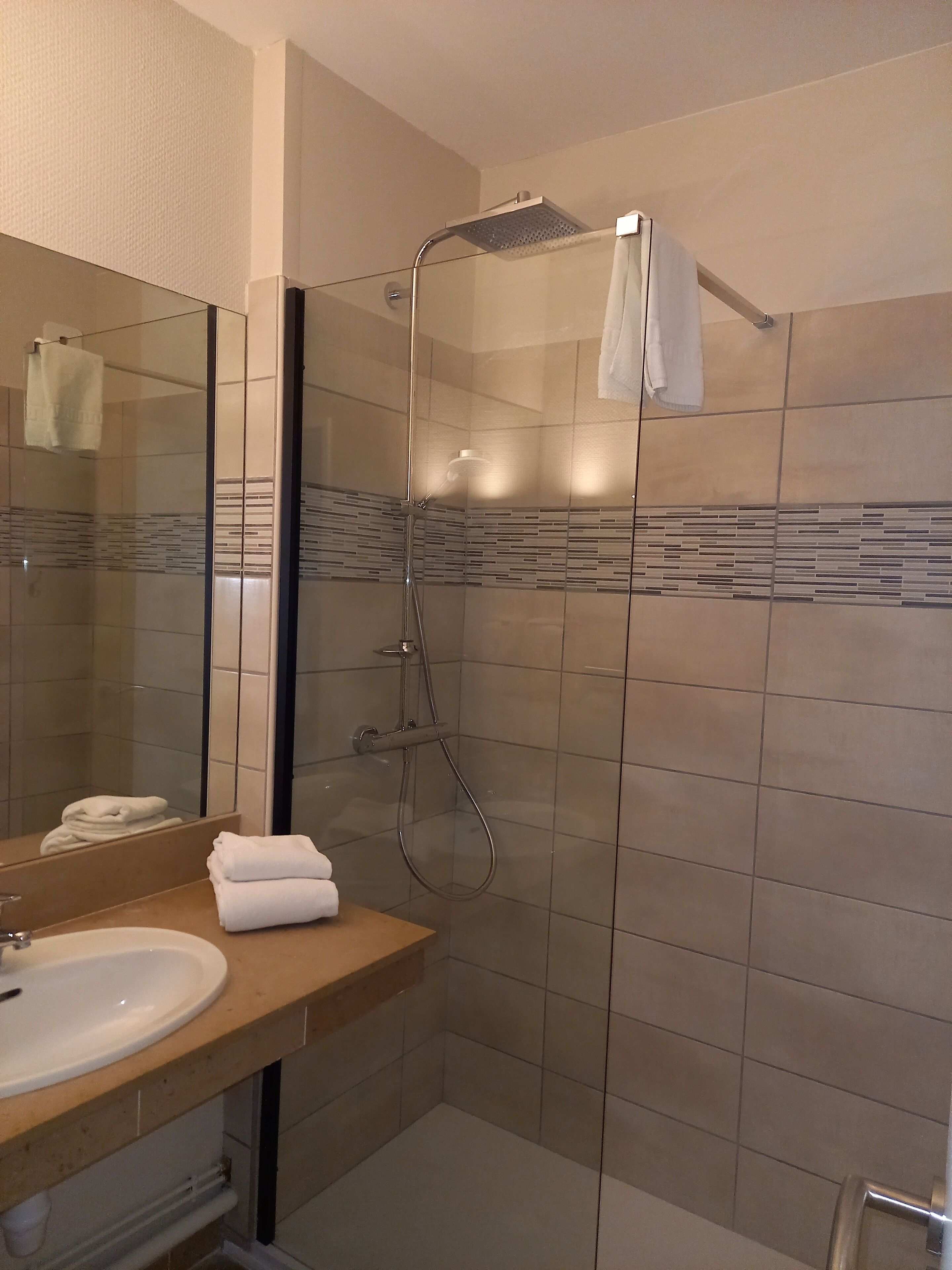 Un baño moderno con ducha de vidrio, un lavamanos con espejo y toallas ordenadamente dobladas.
