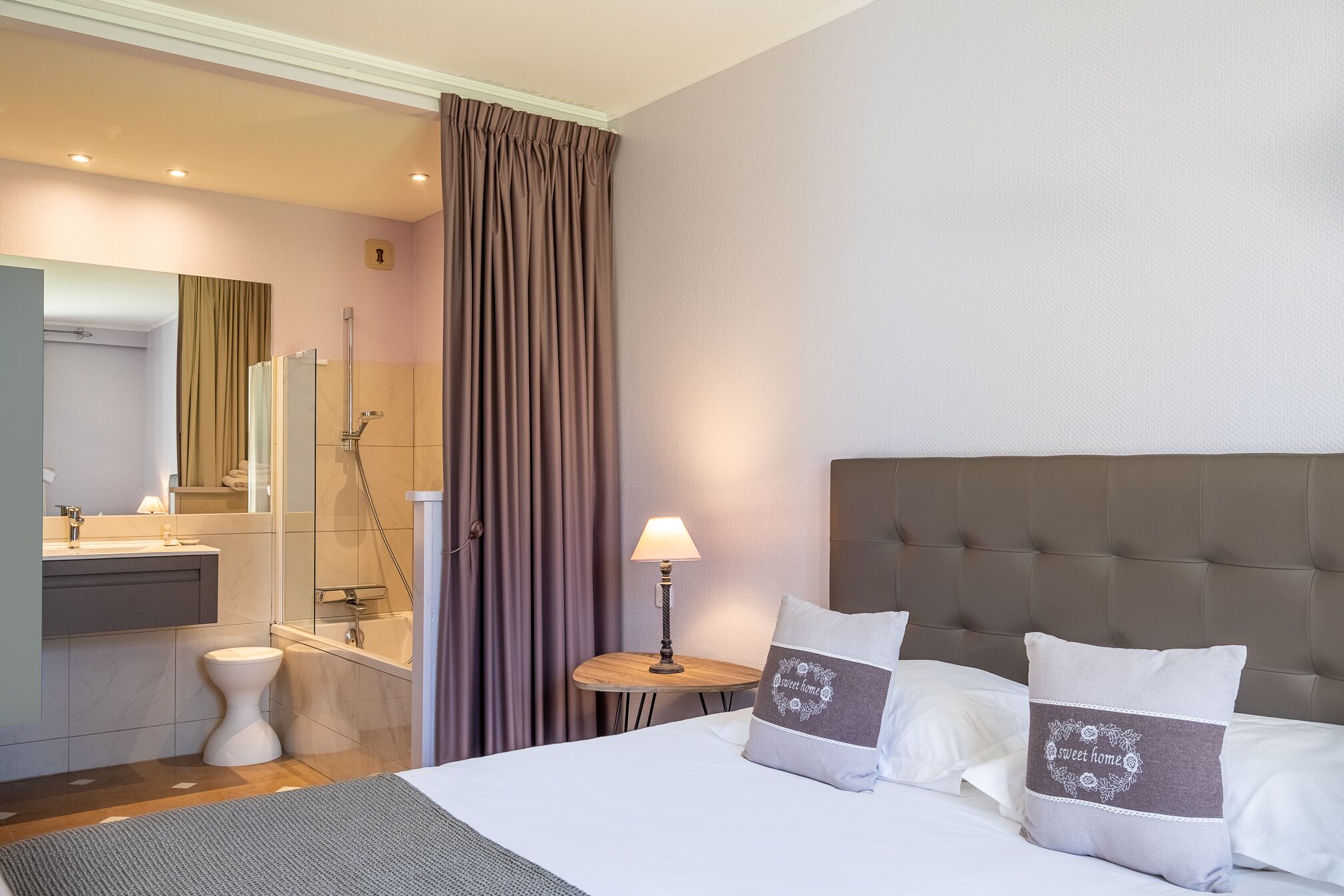Une chambre d’hôtel comprenant un lit, une table de chevet avec une lampe, une salle de bain avec douche et un miroir.