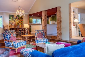 A spacious living room with a large chandelier, wooden chairs, and a vibrant abstract painting on the wall.