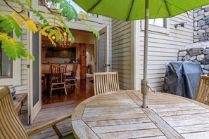 Una terraza exterior de madera con una mesa y sillas, un parasol verde y una pared de piedra.