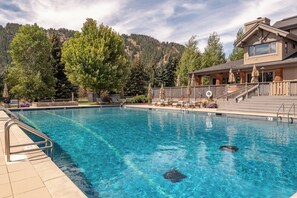 Una piscina cristalina con sillones de descanso y sombrillas, rodeada de árboles y un edificio con balcón.