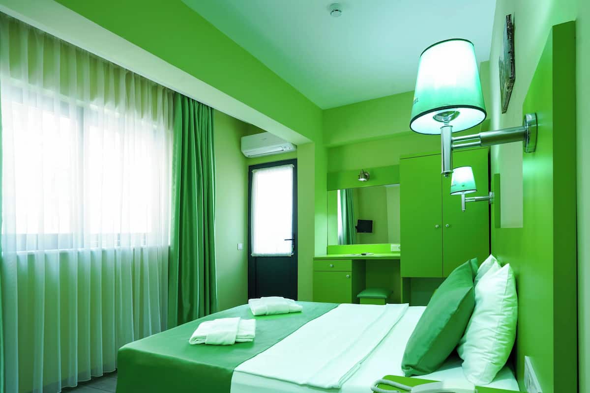 Une chambre d’hôtel avec un lit, une table de chevet avec une lampe, un téléphone et un miroir.