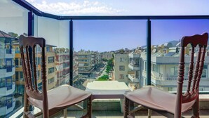 Un balcón con dos sillas de madera y una mesita pequeña, con vista a un paisaje urbano con varios edificios y cielo despejado.