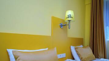 A hotel room with a bed, a bedside table with a phone, a lamp, and a power outlet.