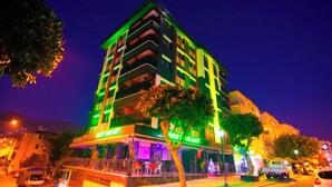 Un hotel de varios pisos con restaurante en la planta baja, balcones y un árbol en la fachada.