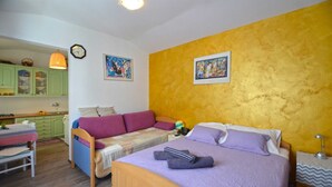 A compact bedroom with a bed, a sofa, a small table, and a kitchen area in the background. - Alan studio Apartment in Rovinj downtown (Rovinj)