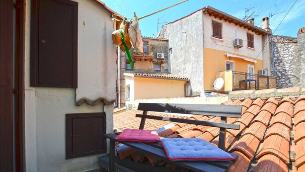 A bench with cushions in a courtyard with terracotta roof tiles and a building with a white facade and brown shutters. - Alan studio Apartment in Rovinj downtown (Rovinj)