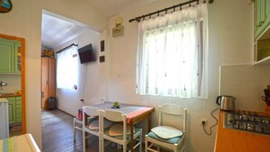 A small, cozy kitchen with a dining table and chairs, a television, and a window with curtains. - Alan studio Apartment in Rovinj downtown (Rovinj)