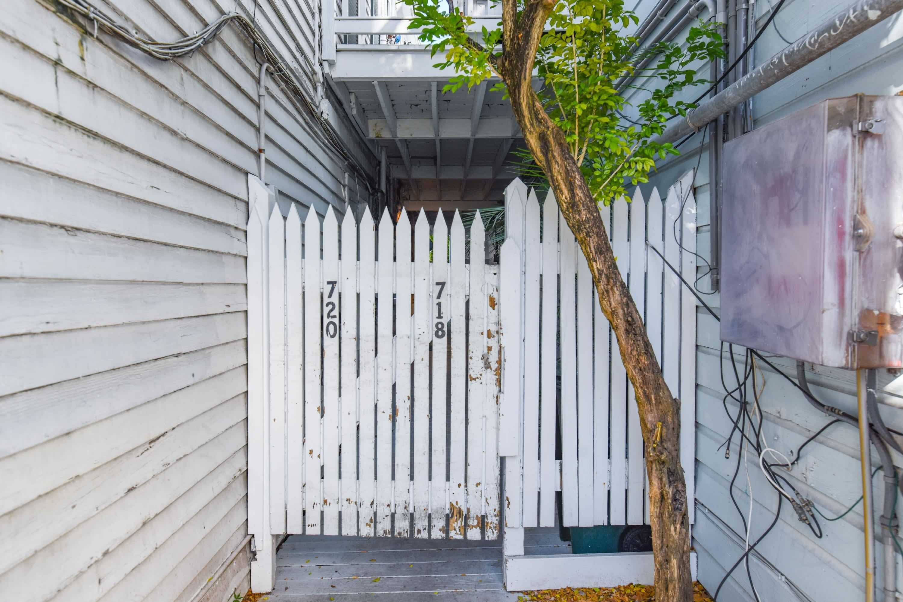 A white picket fence with numbers 720 and 718, a tree, and a building with visible electrical wiring.