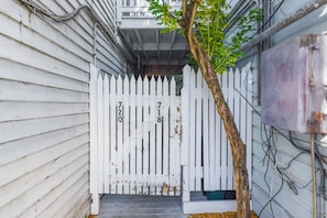 A white picket fence with numbers 720 and 718, a tree, and a building with visible electrical wiring. - Sky Suite with Balcony Overlooking Duval Street (Key West)