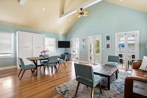 A spacious living room with a high ceiling, wooden flooring, and a dining area with a table and chairs.
