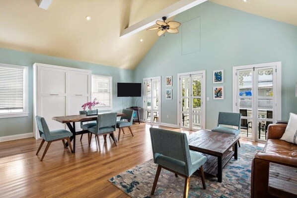 A spacious living room with a high ceiling, wooden flooring, and a dining area with a table and chairs.