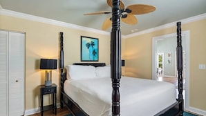 A neatly arranged bedroom with a four-poster bed, a standing fan, and a framed picture on the wall. - Sky Suite with Balcony Overlooking Duval Street (Key West)