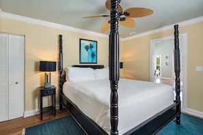 A neatly arranged bedroom with a four-poster bed, a standing fan, and a framed picture on the wall.