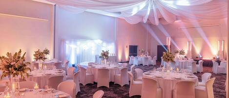 A banquet hall with round tables set for dining, white drapery on the ceiling, and a carpeted floor.
