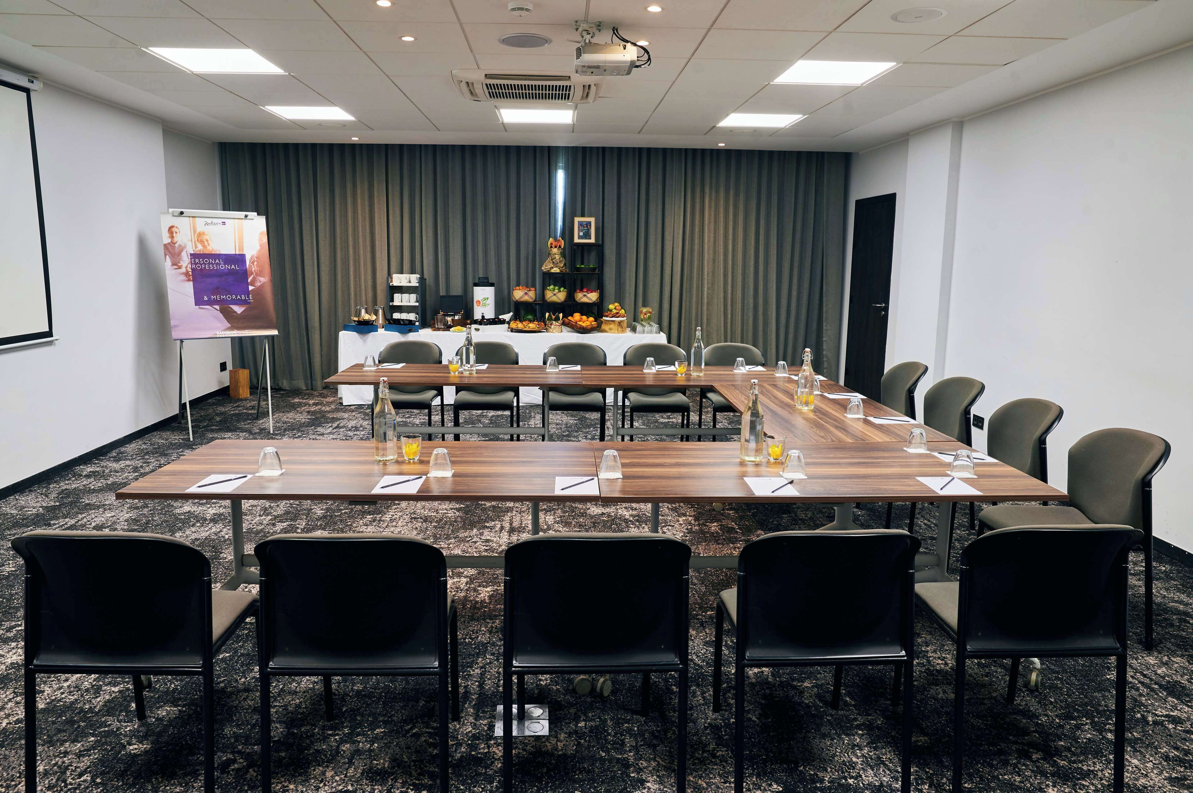 A conference room with a long table, chairs, a projector screen, and a presentation board.