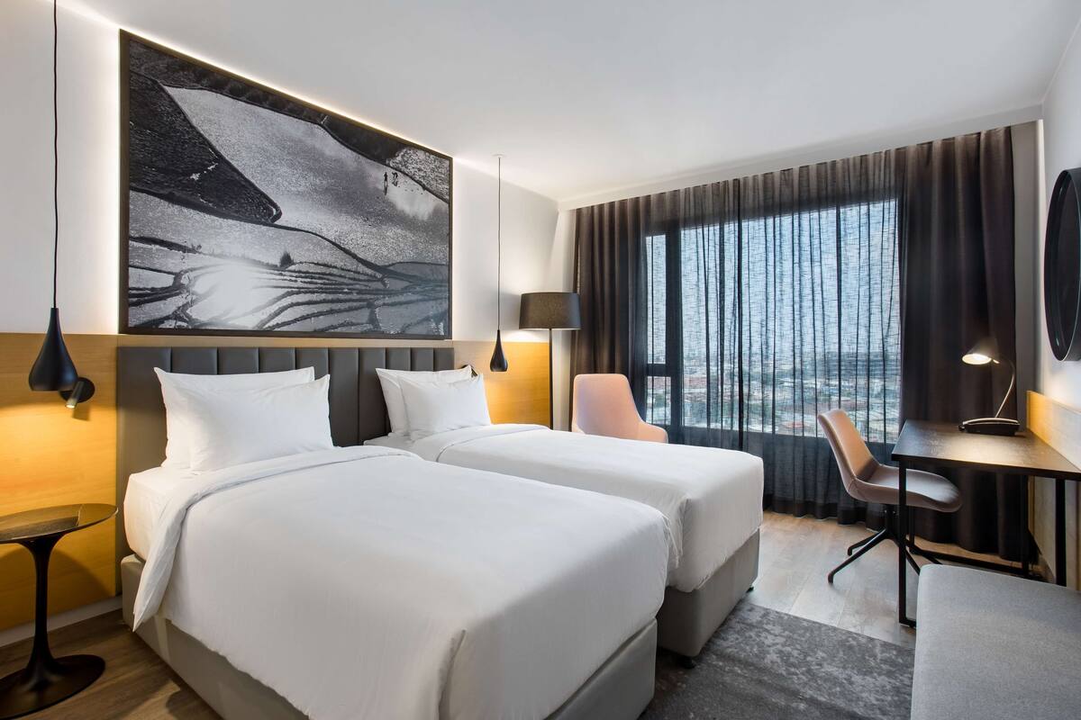 Habitación de hotel con dos camas, un escritorio, una silla y un cuadro grande en la pared.