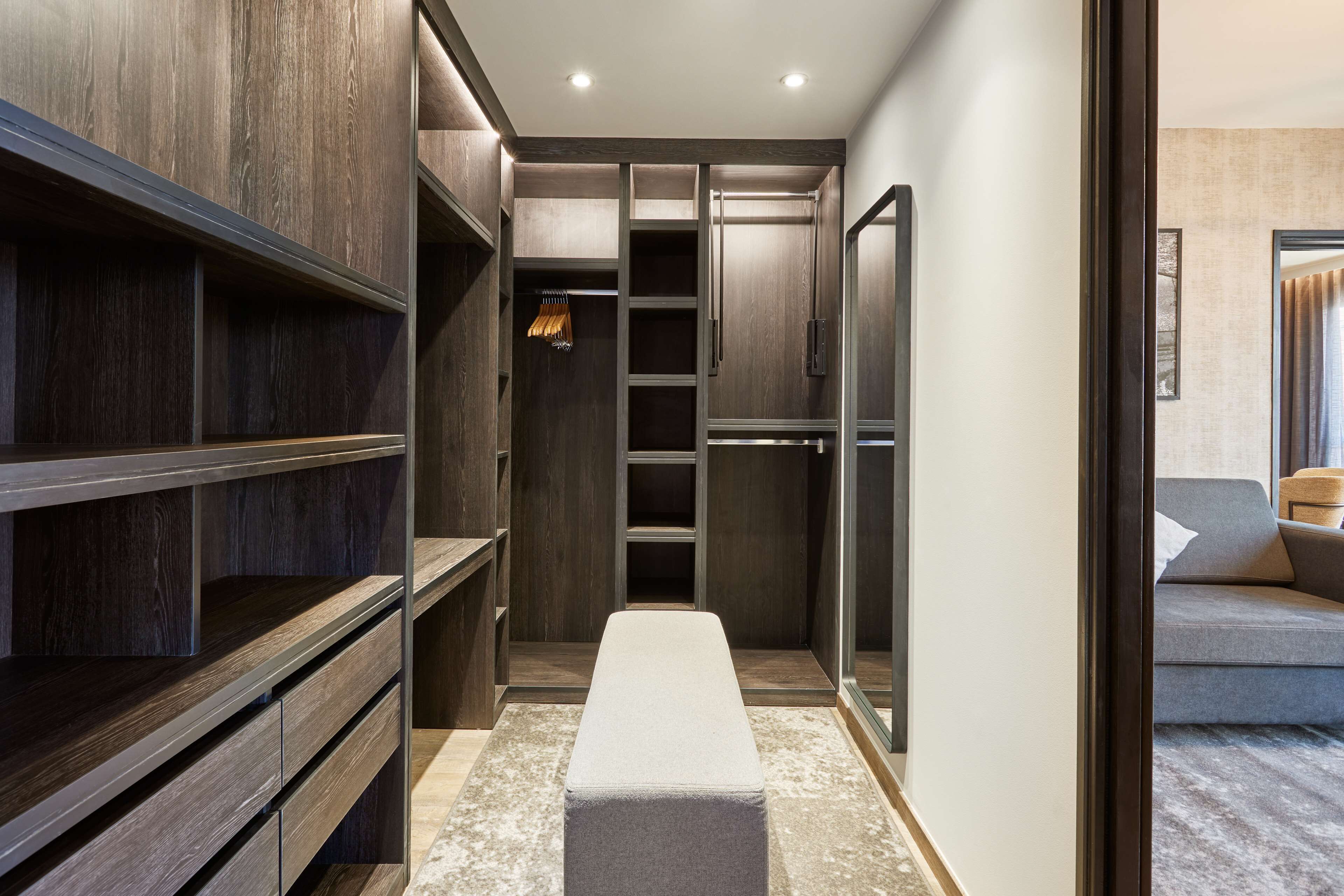 A walk-in closet with wooden shelving, a bench, and a mirrored closet door.