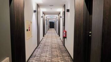 A long, narrow hallway with dark wooden doors on both sides, a patterned carpet, and a fire extinguisher mounted on the wall.