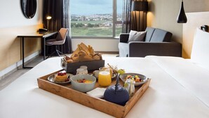 Habitación de hotel con cama, escritorio, silla y bandeja de desayuno con comida y bebidas.