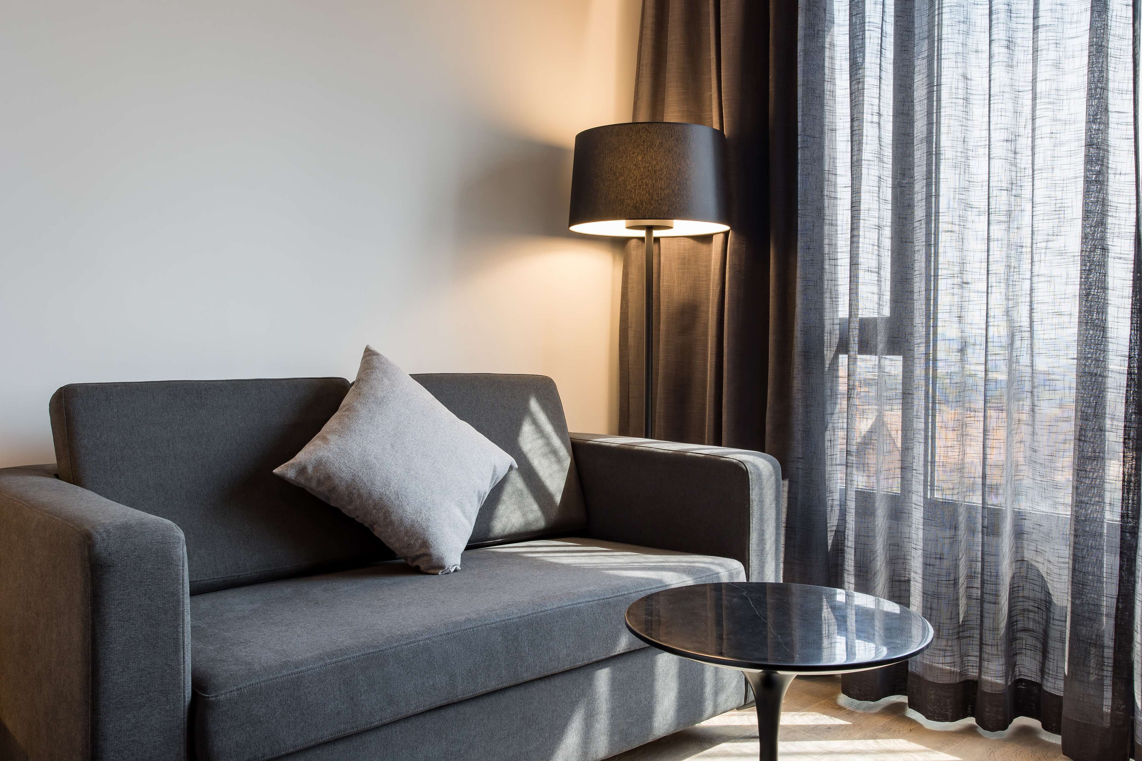 Una sala de estar moderna con un sofá gris, una mesa de centro redonda negra y una lámpara de pie.