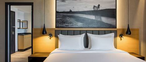 A modern hotel room with a large bed, two bedside lamps, a nightstand, and a large framed picture above the bed.