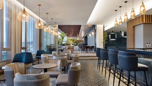 Un moderno vestíbulo de hotel con mesas y sillas redondas, una zona de bar y ventanas amplias que ofrecen vistas.